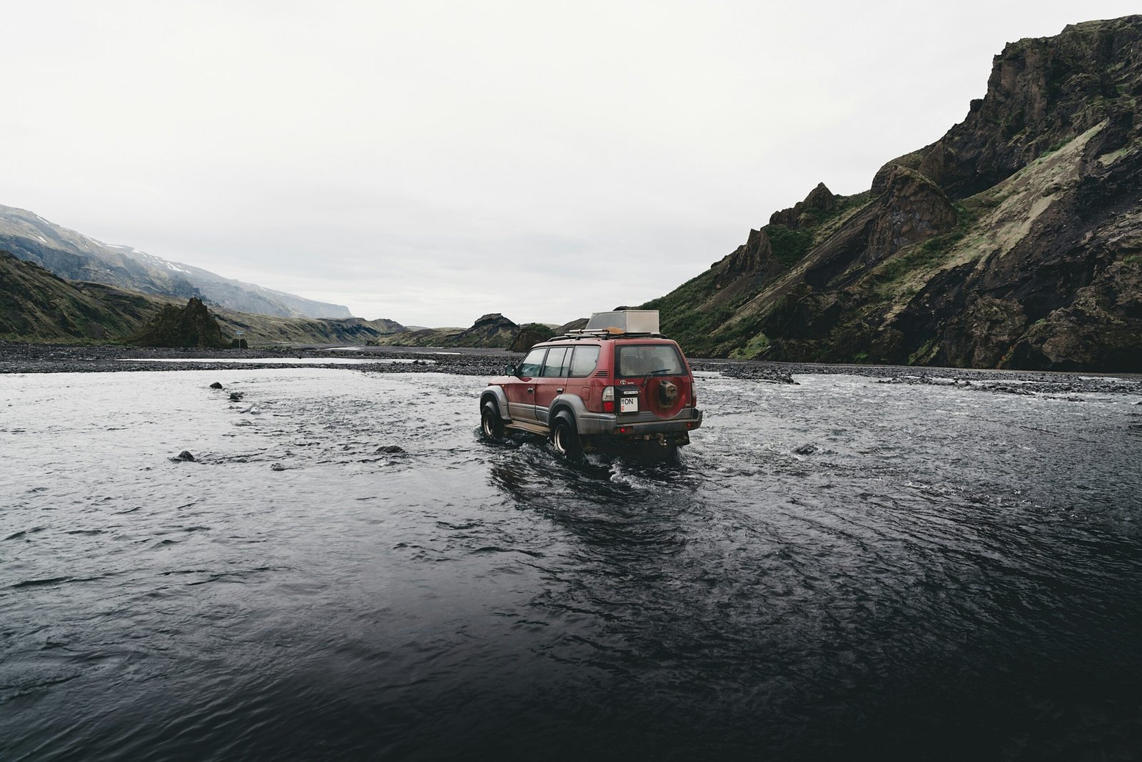 red SUV on water near mountain during daytime